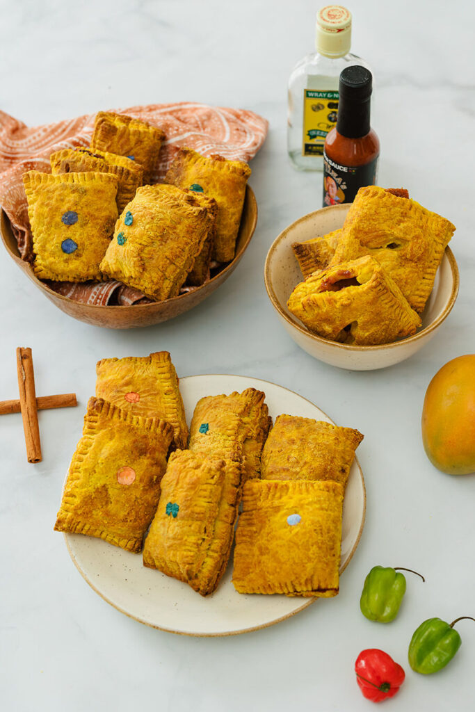 2 bowls and a plate with beef, jerk chicken, mango and rum raisin Jamaican patties on a white table. inKitchener-Waterloo Ontario