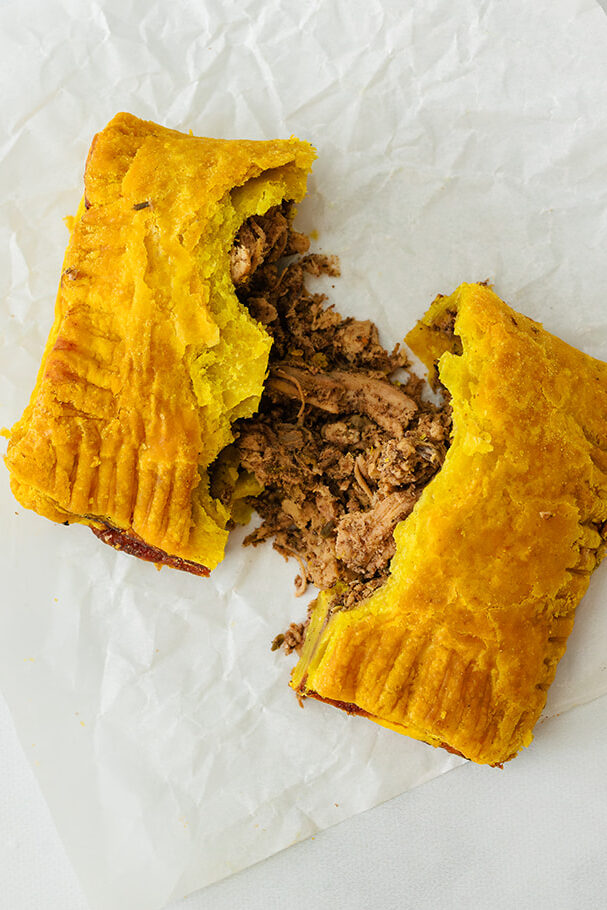 An opened beef Jamaican patty with flaky crust on a white table in Kitchener-Waterloo Ontario